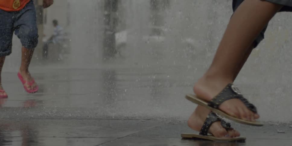 Young people running through spraying water on a sidewalk