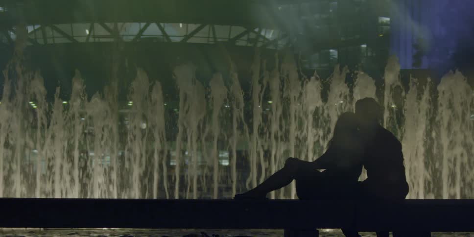 Man and woman sit on a bench and look at a fountain