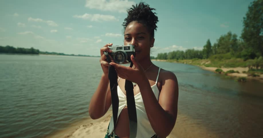 Woman standing on lake shore smiles and takes picture