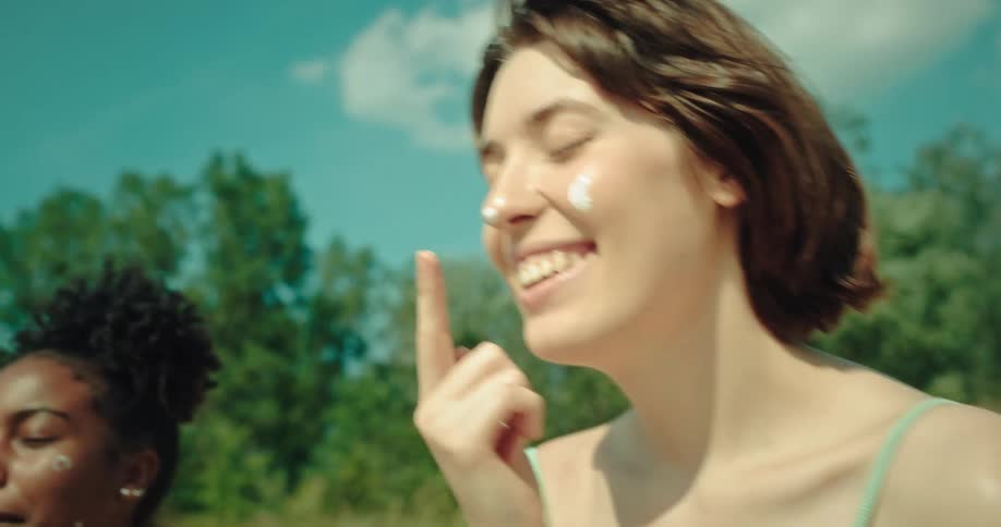 Two young women smile and laugh as they apply sunblock to their faces