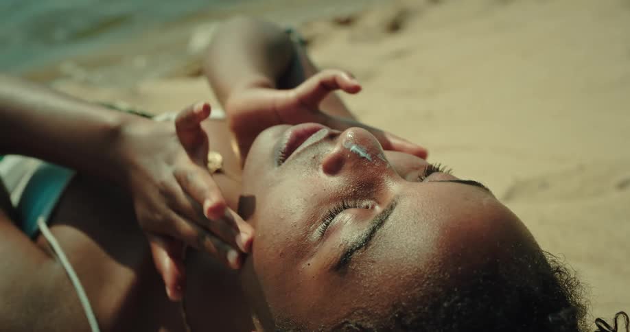 A woman lies on the beach applying sunscreen
