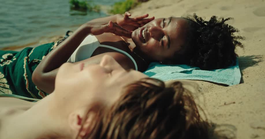 Two friends lying on the sand by the river having a conversation