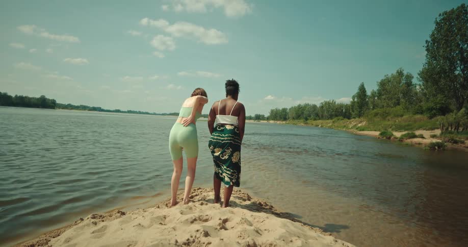 Female friends study lake water while standing on sandy shore