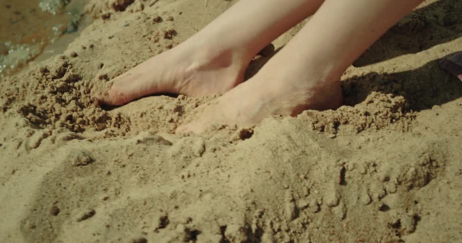 Person burying their toes in the sand at the waters edge during the day