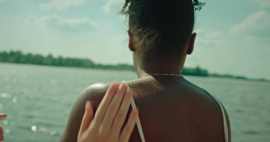 White girl uses sunscreen to put a heart on the shoulder of a black girl and then rubs it in