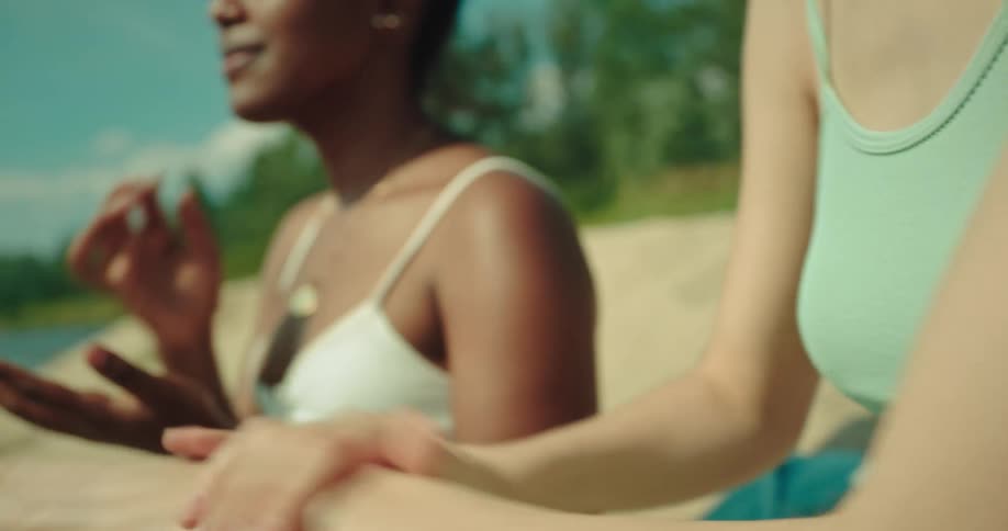 Women sitting on sandy shore apply sunscreen