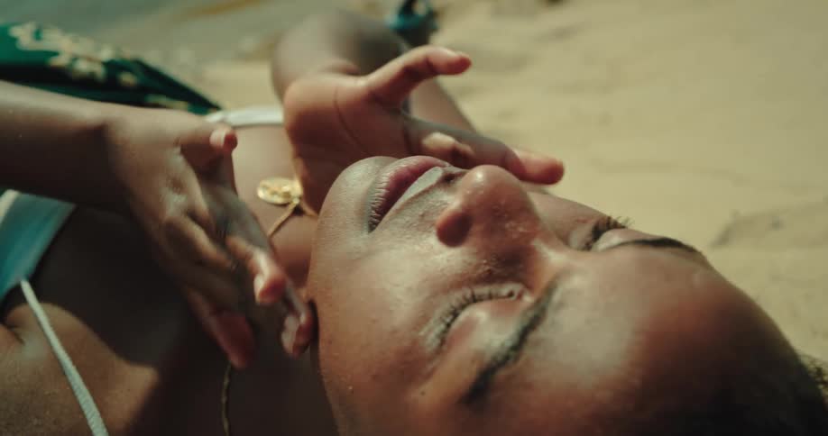 Portrait of a young woman lying on the beach massaging her cheek and arms