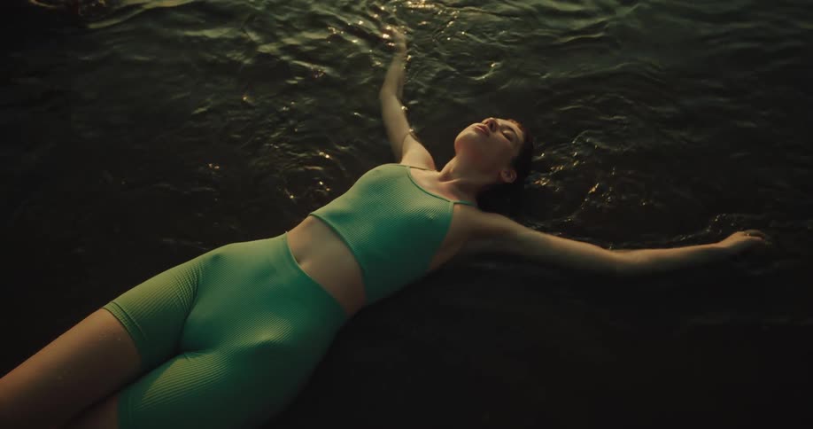 A young woman is lying on her back in shallow water at the beach moving her arms as if she is swimming