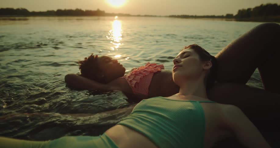 Two women lay together in shallow water that reflects the sun