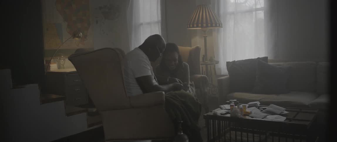A man and woman sit on chairs talking in a living room
