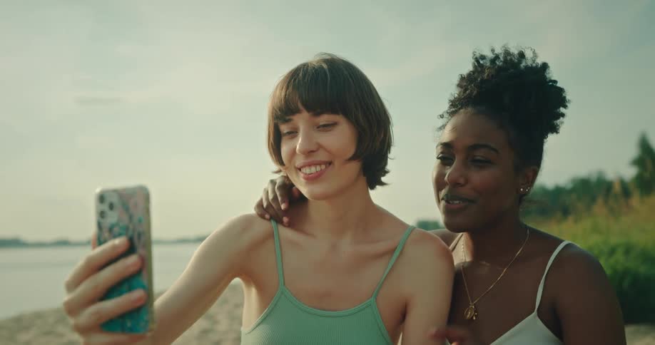 Two friends waving in a selfie on the beach with a cellphone