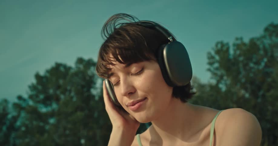 Woman smiles and bobs her head while listening to headphones outdoors