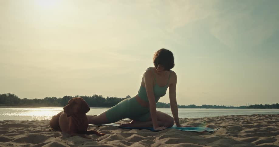 Woman stretching on the beach sand next to her dog