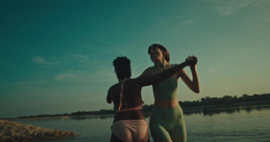 Two friends dancing happily in the middle of a lake with the sunset on the horizon