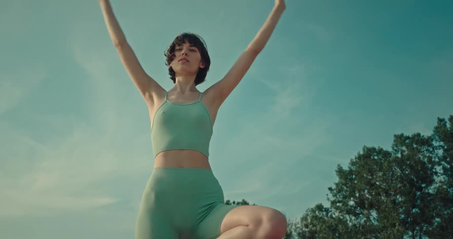 A young woman stands and stretches outdoors on a summer day