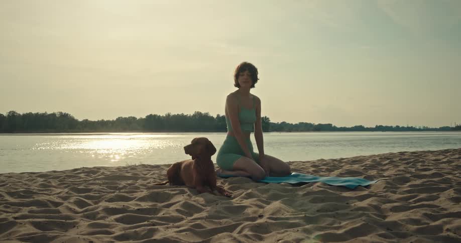 A young woman exercises on the beach with her dog lying next to her