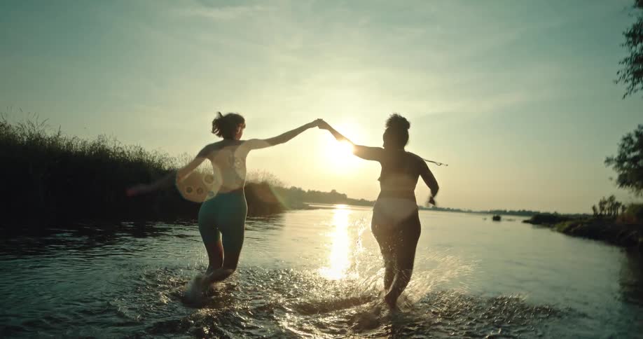 Two women hold hands and run in the water