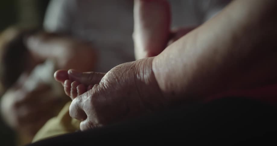 Older persons hand is grabbing a babys foot while the mom holds the babys head and smiles