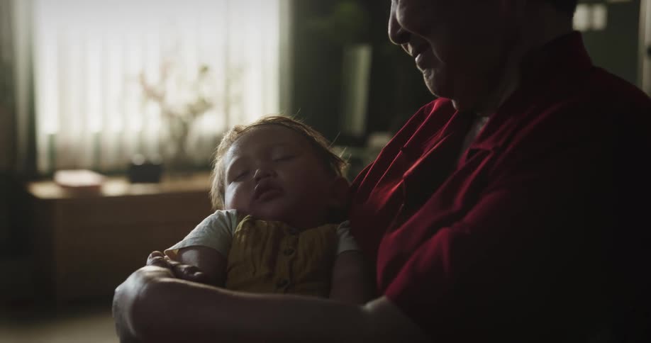 A sleeping baby is being held by her grandmother
