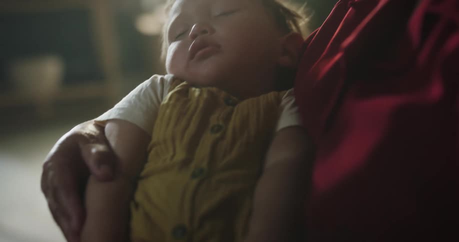 Elderly woman holding a baby in her arms with sunlight reflection in the background in an indoor setting