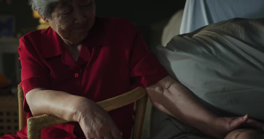 Grandmother sits by bed and strokes head of sleeping grandchild