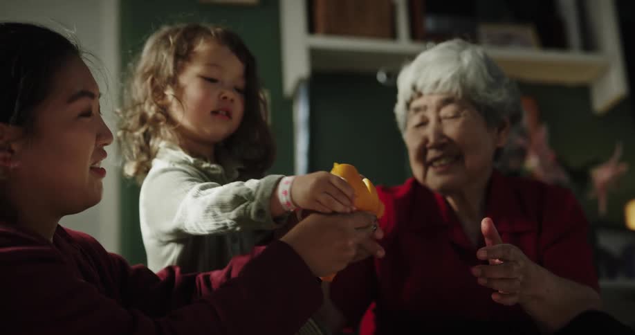 Grandmother peeling an orange for her granddaughter with her daughter beside them