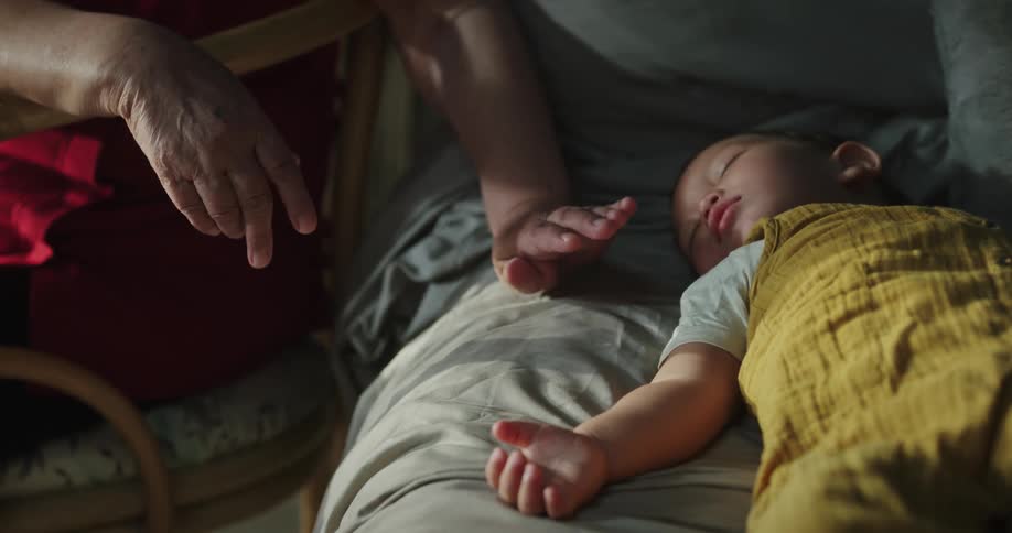 A toddler is sleeping while an elderly person paths him