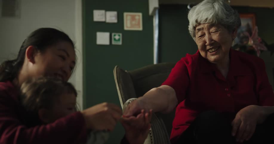 Mother and daughter painting the nails of the lady sitting in the armchair