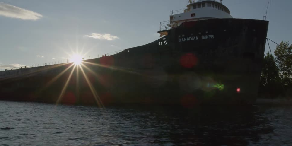 Passing view of a large ship as the sun shines behind it as it's setting