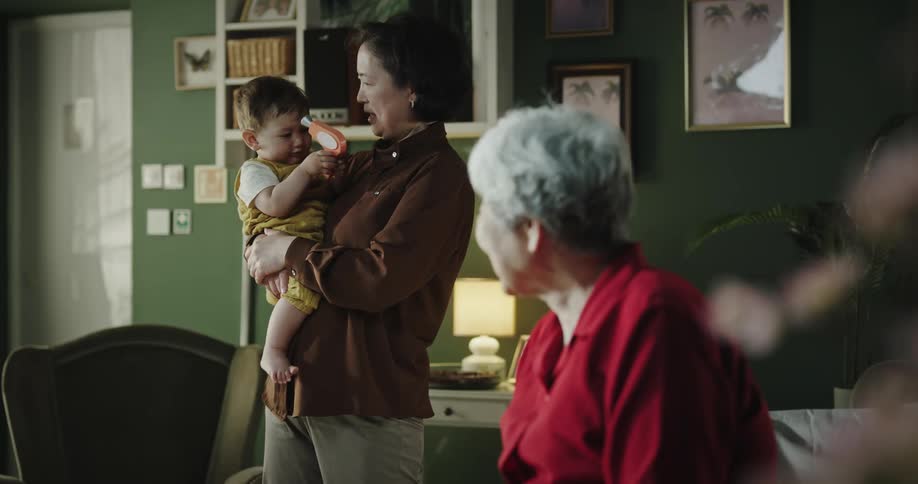 A clip of a family consisting of a male and female toddler a grandmother and the mother in a sitting room