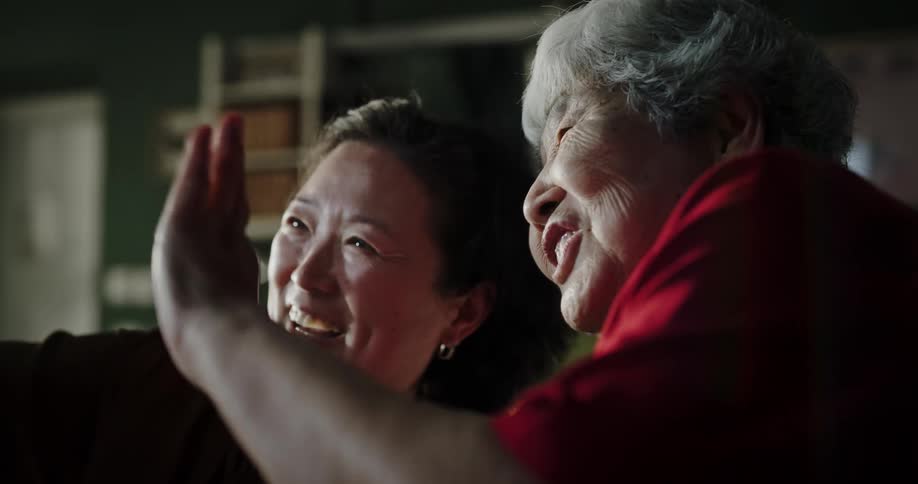 Elderly mother and daughter wave at smartphone during a video call in their home