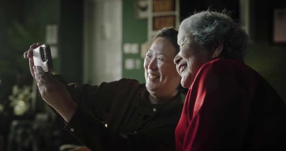Two old women are making a video call on their cell phones and wave at the camera