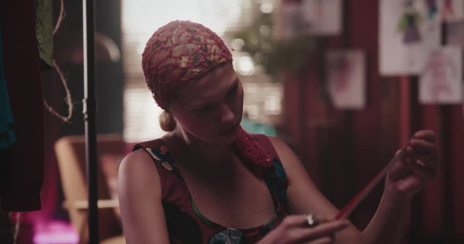Woman examines a ribbon before handing it to another woman who is using a sewing machine