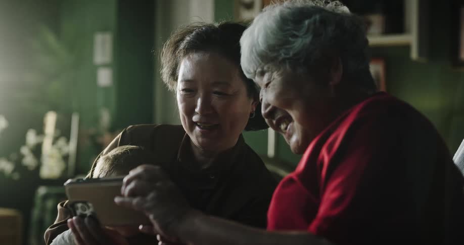 Elderly woman taking a selfie with her daughter who is holding a baby