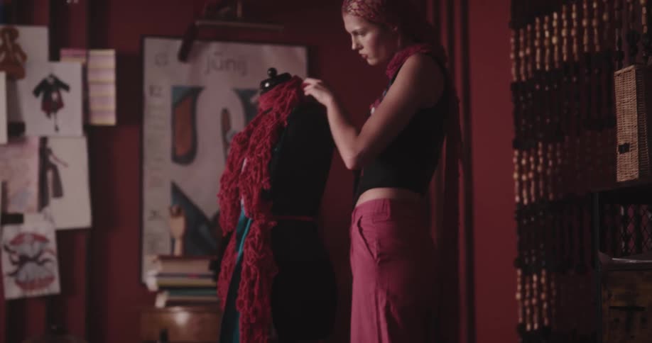 Woman placing scarves on a mannequin and another sitting on the floor sketching fashion designs