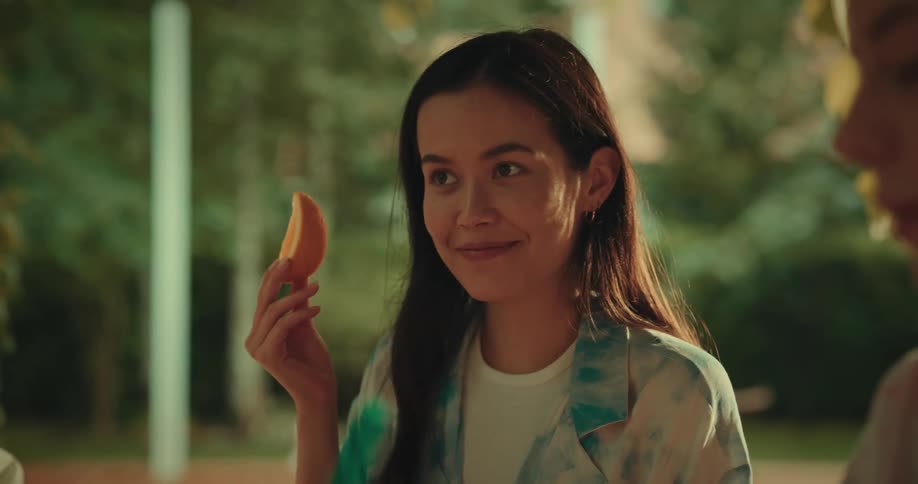 A woman holds up her food while smiling at a table with others