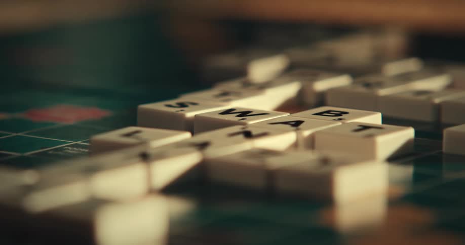 Someone playing scrabble putting pieces on the board to form words