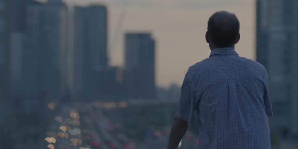 A man stares out onto a city road with tall buildings in the background