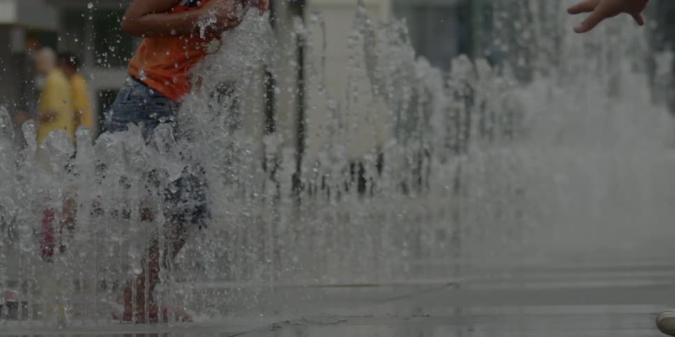 People play in the sidewalk water fountains
