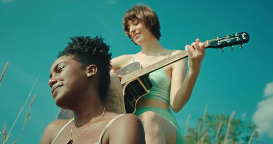 Woman enjoys the music while her friend plays a guitar as they sit outdoors in field