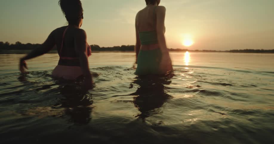 Lesbian couple wearing bikinis go swimming at sunset