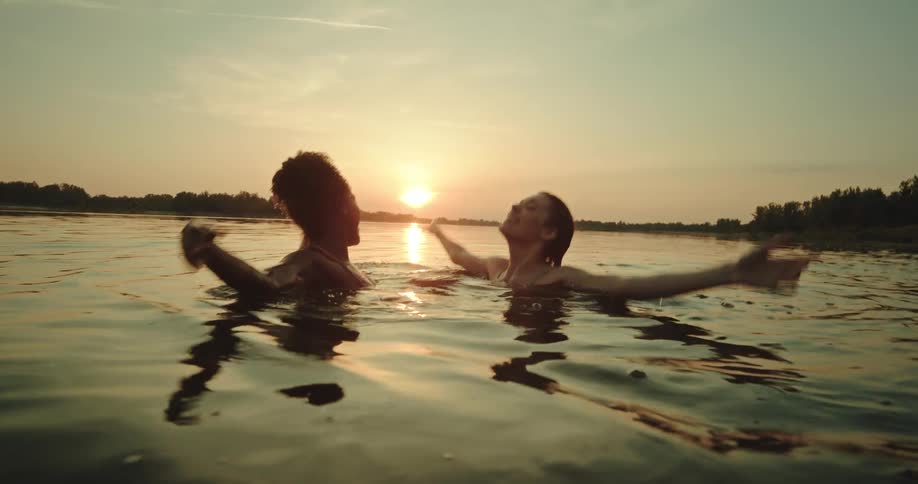 Two females move and dance shoulder deep in ocean lake