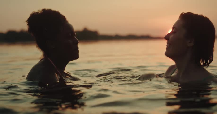 Two women play in the water at sunset