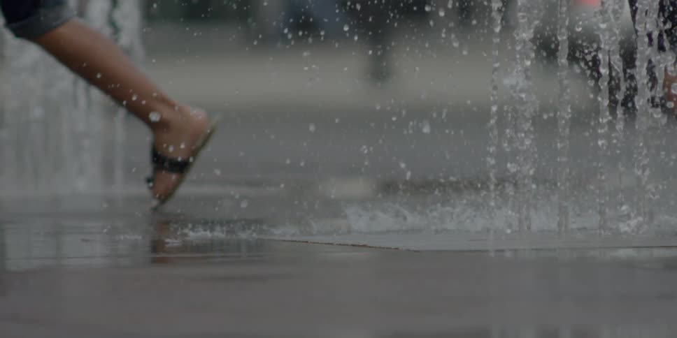 Kids in flip flops run through a fountain