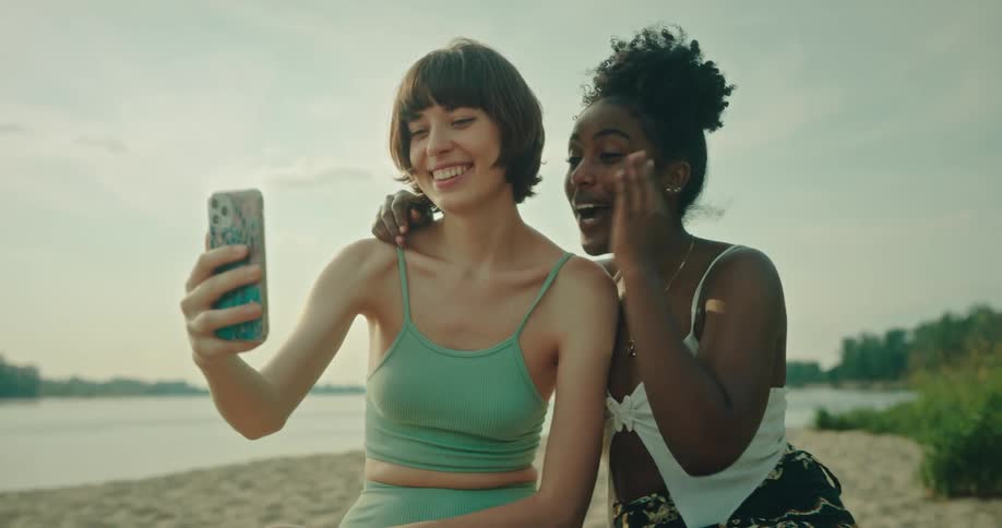 Portrait of two friends at the beach having a conversation in a selfie with a cellphone