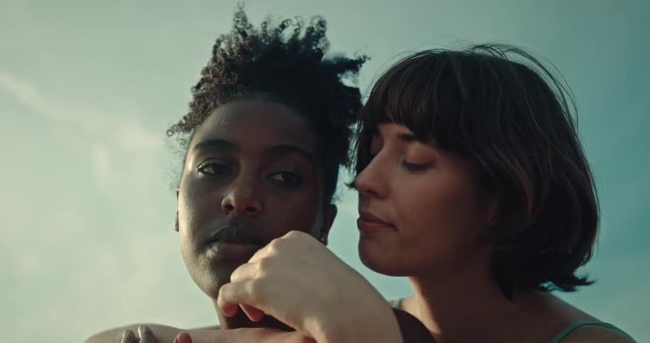 Women cuddle outside on a windy day stroking each others skin