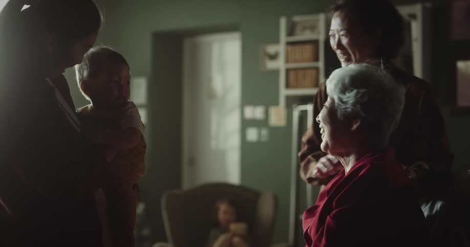 An elderly woman is sitting and is happy when she sees some people with a small baby on her lap