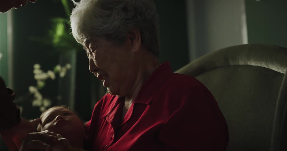 Elderly woman wearing a red shirt holds toddler baby crying
