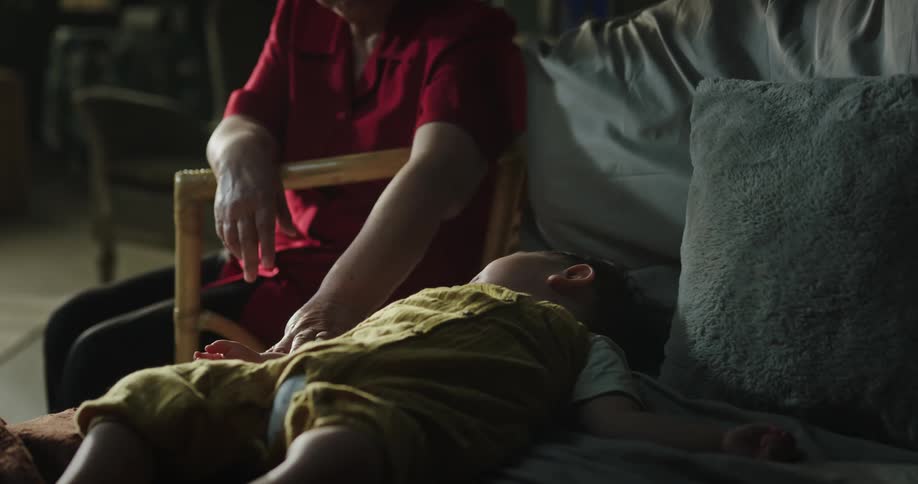 Elderly woman caressing a baby sleeping indoor on the chair during the day