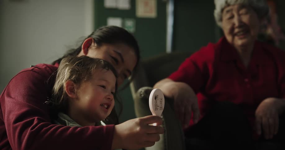 Two asian women sit with toddler and smile and gesture